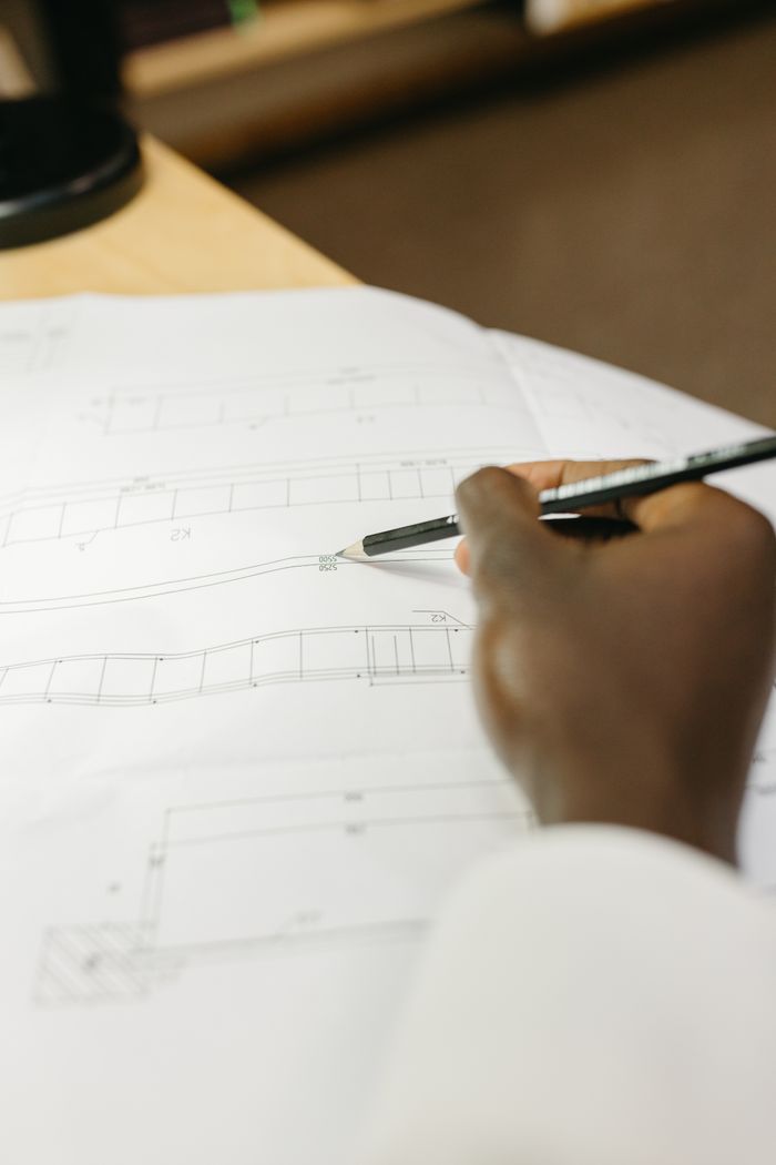 Detailed view of an architect's hand drafting a blueprint in a workspace setting.